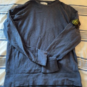 Blå långärmad tröja från Stone Island  - Säljer en blå långärmad tröja från Stone Island med klassisk patch på ärmen. Tröjan har rund halsringning och är tillverkad i mjukt material, perfekt för en avslappnad stil. Storlek medium men passar small.