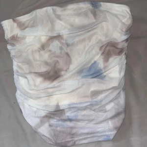 Tubtopp i tie-dye mönster - Säljer en tubtopp med vitt och ljusblått tie-dye mönster. Toppen är axelbandslös och har en lätt rynkad effekt som ger en snygg passform. Perfekt för sommardagar eller festivaler!