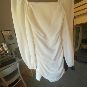 Vit långärmad klänning med puffärmar - Säljer en vit klänning med långa, dramatiska puffärmar och rynkade detaljer framtill. Klänningen har en fyrkantig ringning och är figurnära med snygg drapering nedtill. Perfekt för dig som vill sticka ut!