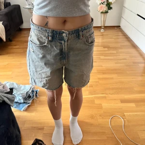 Ljusblå jeansshorts med fransar från Zara - Säljer ett par ljusblå jeansshorts från Zara med råa fransade benslut och klassisk femficksmodell. Shortsen har normal passform och är tillverkade i denim. Perfekta för sommaren!