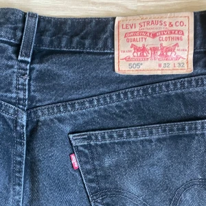 Levi's 505 svarta jeans W32 L32 - Svarta Levi's 505 jeans med regular fit och raka ben. Klassisk femficksmodell med dragkedjegylf och råa, fransiga benslut. Tillverkade i 100% bomull och har den ikoniska läderpatchen bak i midjan.