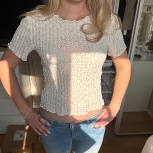 Vit croppad topp med volangkant - Säljer en söt vit croppad topp med korta ärmar och volangkant. Toppen har ett virkat, ribbat mönster och är stretchig. Perfekt till jeans eller kjol för en fräsch look.