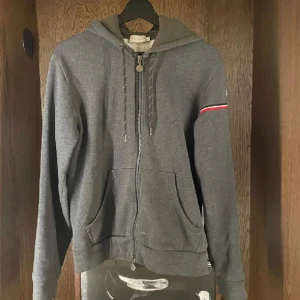 Moncler hoodie grå - Säljer en grå hoodie från Moncler med dragkedja framtill och två fickor. Skicket är väldigt bra och tröjan är i storlek M men passar mer som S 