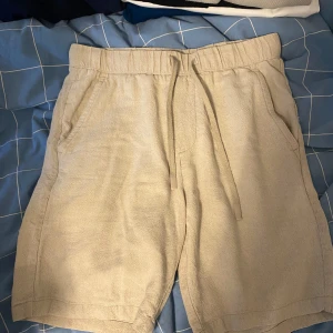 Beiga linneshorts från Zara - Säljer ett par beiga shorts från Zara i linne med normal passform. De har resår i midjan och snörning samt två sidofickor. Perfekta för varma dagar och en avslappnad stil.