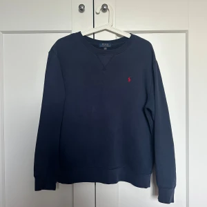 Mörkblå sweatshirt ifrån Ralph Lauren - En super fin sweatshirt i marin blått tyg med röd Ralph Lauren logga på framsidan! Fint skick! Finns dock en liten slitning på framsidan. Storlek 14-16 barnstorlek men passar S! 