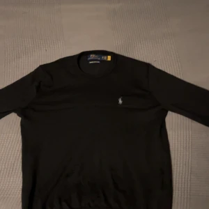 Svart merinoullströja från Polo Ralph Lauren - Säljer en klassisk svart långärmad tröja från Polo Ralph Lauren i mjuk och tvättbar merinoull. Säljs för att det inte passar längre. Hör av dig vid minsta fundering!