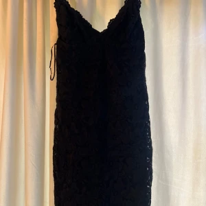 Svart spetsklänning från New Yorker - Säljer en svart kortklänning från New Yorker med smala axelband och v-ringad urringning. Klänningen har ett lager av spets över hela och en figurnära passform. Perfekt för dig som gillar en klassisk och stilren look.