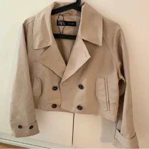 Beige trenchcoat  - Säljer en beige trenchcoat från Zara. Jackan har långa ärmar och dekorativa knappar vid ärmsluten. Perfekt för vår och höst.