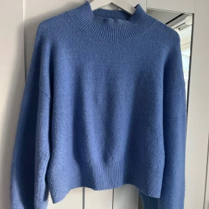 Blå stickad tröja från & Other Stories - Mysig blå stickad tröja från & Other Stories med hög krage och ribbade muddar vid ärmslut och nederkant. Perfekt för lager-på-lager under kyliga dagar, bland annat under sommaren. Lite använd men fortfarande i bra skick. Skicka för fler bilder💙