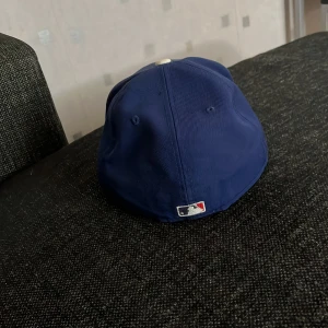 Blå keps från New Era - Säljer en blå keps från New Era, modell 59FIFTY. Kepsen har en vit LA-logga på framsidan och är en del av MLB Authentic Collection. Den är i storlek 7 3/8 (58.7 cm) och har en böjd skärm. Perfekt för sommarens alla äventyr!