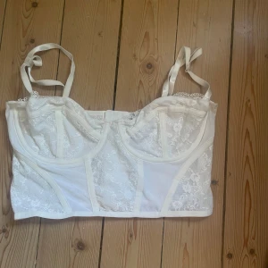 Vit spetskorsett från H&M Divided - Säljer en vit korsett-topp från H&M Divided med spetsdetaljer och reglerbara axelband. Toppen har bygel och hakknäppning bak. Den är i storlek M men passar även S, aldrig använd✨💕