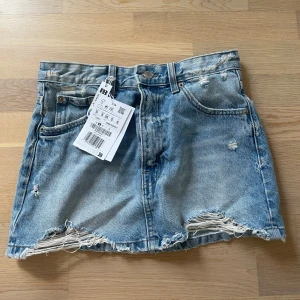 Blå jeanskjol från Pull&Bear - Säljer en blå jeanskjol från Pull&Bear med råa, slitna kanter och distressed detaljer. Kjolen har klassisk femficksdesign och bälteshällor. Perfekt för en avslappnad stil. Helt oanvänd. 