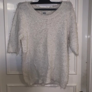 Vit fluffig stickad tröja från Vero Moda - Mysig vit stickad tröja från Vero Moda med fluffig textur. Tröjan har rund halsringning och trekvartsärmar, perfekt för lager-på-lager-stil under kyligare dagar.