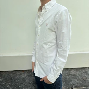 Polo Ralph Lauren skjorta - Klassisk vit skjorta från Polo Ralph Lauren med broderad logga på bröstet. Slim fit-modell med långa ärmar och knappar hela vägen framtill. Perfekt till jeans eller chinos för en clean och stilren look.