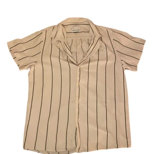 Samsøe Samsøe skjorta - Snygg beige/cremevit skjorta från Samsøe Samsøe med mörkgröna vertikala ränder och klassisk krage. Skjortan har korta ärmar och knäppning framtill, perfekt för en avslappnad och stilren look. 