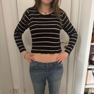 Svart croppad långärmad tröja med vita ränder - Säljer en svart croppad långärmad tröja med vita horisontella ränder. Tröjan har en enkel rund halsringning och är i ett mjukt, stretchigt material. Perfekt till jeans eller kjol för en avslappnad stil.