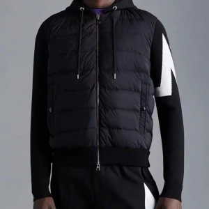 Svart Moncler jacka herr - Svart dunväst med huva och dragkedja framtill från Neil Barrett. Västen har quiltad design och två fickor med knappstängning. Ärmarna har en vit blixtdetalj som ger en cool kontrast.