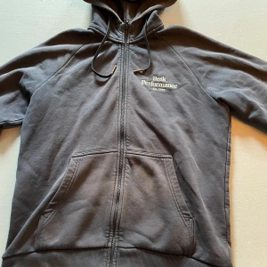 Mörkblå hoodie från Peak Performance - Säljer en mörkblå hoodie från Peak Performance med dragkedja och huva. Tröjan har fickor framtill och logga broderad på bröstet. Perfekt för en avslappnad stil och enkel att matcha med andra plagg. Tröjan är delvis solbränd men detta är inget som påverkar funktionen! Storlek L