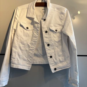 Vit jeansjacka från Object - Säljer en klassisk vit  jeansjacka från Object i storlek 38. Jackan har svarta knappar framtill och på bröstfickorna, samt lång ärm och krage. Perfekt för vår och sommar💕