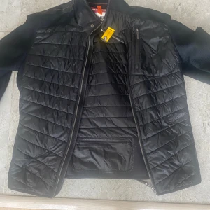 Svart quiltad jacka från Parajumpers - Säljer en svart quiltad jacka från Parajumpers i storlek M. Jackan har dragkedja, ståkrage och en bröstficka med dragkedja. Materialmix med glansig polyester framtill och bak samt stickade partier på ärmar och sidor.