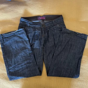 Vida Lågmidjade jeans - Skitsnygga jeans från Jeans Hearts med vida ben och låg midja. Har lite slitage nedtill vid benet (se bild) men är annars i väldigt bra skick. Jeansen är i lite tunnare material vilket gör de perfekt till sommaren! Mått: midja 40-41 längd: 97 Skriv vid frågor eller liknande🥰