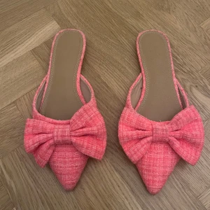 Rosa slip-in sandaler med rosett - Säljer ett par rosa sandaler med spetsig tå och stor rosett framtill