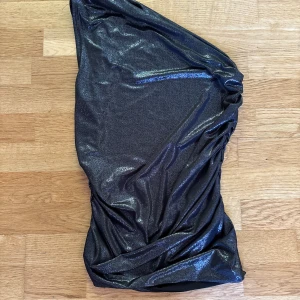 Fest klänning - Glittrig svart one shoulder klänning från H&M. Klänningen har en asymmetrisk design med en axel. Materialet är stretchigt och skimrande.