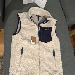 Beige fleeceväst från Patagonia. HELT NY! - HELT NY!!! Säljer en vit fleeceväst från Patagonia med marinblå detaljer och dragkedjor. Västen har en bröstficka med dragkedja och två sidofickor, samt hög krage. Perfekt för lager-på-lager och outdoor, en skön sommarkväll eller höst. Jätteskönt material på både insidan och utsidan. Storlek S. Skick 10/10 Nypris: 1400kr, Mitt pris ENDAST: 1199kr      Hör gärna av er vid funderingar eller fler bilder 😊