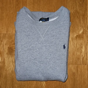Grå sweatshirt från Polo Ralph Lauren - Klassisk grå sweatshirt från Polo Ralph Lauren med rund halsringning och broderad marinblå logga på bröstet. Perfekt basic-tröja med normal passform och mjukt material.