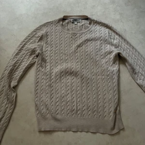 Beige kabelstickad tröja från Hampton Republic - Säljer en klassisk beige kabelstickad tröja från Hampton Republic. Tröjan har rund halsringning och långa ärmar, perfekt för lager-på-lager. Stilren och enkel att matcha till olika outfits.