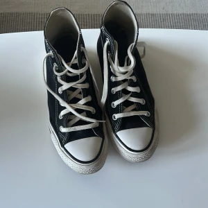 Svarta Converse Chuck Taylor All Star - Klassiska svarta Converse Chuck Taylor All Star high-top sneakers med vit sula och tå, vita snören och tydliga loggor på sidan. Perfekta för dig som gillar en tidlös och avslappnad stil.