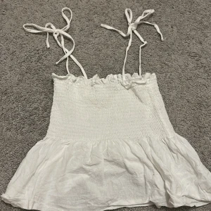 Vit croppad linnetopp från SHEIN - Säljer en söt vit croppad linnetopp från SHEIN med smockad överdel och volang nertill. Toppen har tunna axelband som är justerbara då man kan knyta om de. Perfekt för varma dagar. Skriv gärna innan köp eller om du har någora frågor!💗