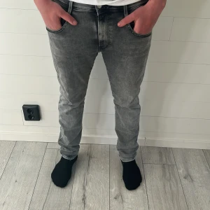 Gråa Replay jeans hyperflex - Säljer ett par grå jeansbyxor från Replay i klassisk femficksmodell. Byxorna har normal passform och raka ben, med snygga slitningar och svarta detaljer vid linningen. Perfekta för en stilren och avslappnad look.| Skriv vid intresse |