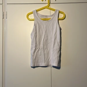 Vit ribbad linnetopp - Säljer en klassisk vit ribbad linnetopp i bomull. Perfekt basplagg med rund halsringning och ärmlös design. Enkel och stilren modell som passar till det mesta.