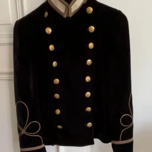 Svart sammetsjacka med guldknappar från Ralph Lauren - Säljer en svart sammetsjacka från Denim & Supply Ralph Lauren. Jackan har dubbelknäppning med guldknappar och dekorativa broderier i guld på ärmarna. Stilig militärinspirerad look med ståkrage och unika detaljer.