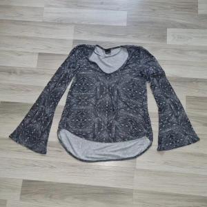 Gråmönstrad långärmad topp från Gina Tricot - Säljer en grå långärmad topp från Gina Tricot med vitt geometriskt mönster. Tröjan har v-ringning och utsvängda ärmar för en cool look. Tunt och mjukt material som passar perfekt till många outfits.