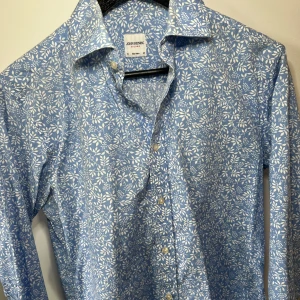 Blå  skjorta från John Henric - Snygg blå skjorta från John Henric med vitt blommigt mönster. Skick 8/10 säljer pga för liten, passar small. Köpt för 800kr i affär säljer för 250kr. 