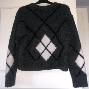 Mörkgrå stickad tröja med rutmönster från XOXO friends - Mysig mörkgrå stickad tröja från XOXO friends med vita och svarta rutor i ett argylemönster på både fram- och baksida samt ärmar. Suuuuuper mysig och tjock tröja som jag älskar att ha på vibrern men vill förnya min garderob! Skriv vid frågor som ch fubderingar!💓