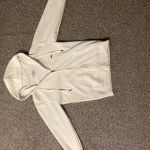 Vit zip hoodie från Lacoste - Säljer vi lacoste zip hoodie som jag fått i julas tror den är äkta använt den några gånger och säljer för att den inte passar längre. 
