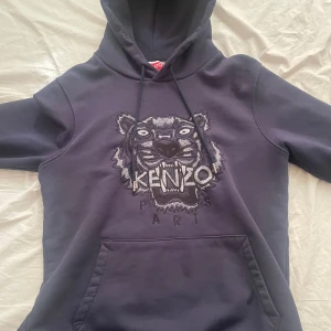 Mörkblå hoodie från Kenzo med tigerbroderi - Säljer en mörkblå hoodie från Kenzo. Tröjan har huva med dragsko och en stor magficka. Perfekt för dig som gillar streetwear och vill sticka ut med en snygg detalj. Använt ett par gånger bara. Pris går att diskuteras!