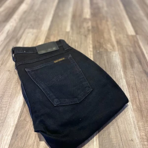 Svarta jeansbyxor från Nudie Jeans - Snygga svarta jeans från Nudie Jeans med klassisk femficksdesign, svarta sömmar.  W27 L32.     Flertal mer jeans i profilen 