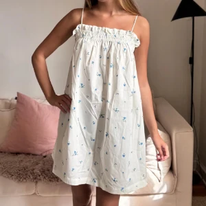 Vit blommig sommarklänning med smala axelband - Söt vit klänning med små blå blommor och smala axelband. Superfin!!!