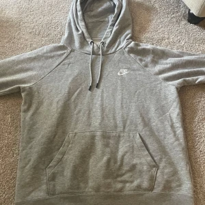 Grå hoodie från Nike - Säljer en klassisk grå hoodie från Nike med vit logga på bröstet. Tröjan har huva med dragsko och en stor magficka framtill. Perfekt för en avslappnad stil och enkel att matcha med det mesta.