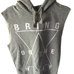 Grå ärmlös hoodie med tryck - Grå ärmlös hoodie med vit text och grafiskt tryck på framsidan. Huva med dragsko och mjukt material, perfekt för en avslappnad stil.