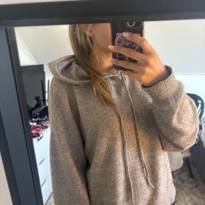 Beige stickad hoodie med huva - Mysig beige stickad hoodie med huva och snörning. Tröjan har en relaxed fit och långa ärmar med ribbade muddar. Perfekt för kyliga dagar när du vill vara både bekväm och snygg.