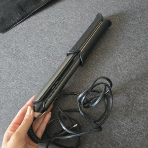 Svart och guld plattång - En stilren plattång i svart och guld med sladd. Ergonomiskt handtag och enkel att använda med knappreglage på sidan. Endast för raktang – ej locktång.