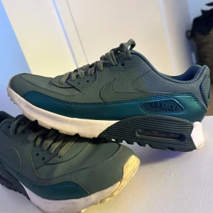 Nike Air Max 90 i mörkgrönt - Snygga Nike Air Max 90 sneakers i en mörkgrön färg med matchande snörning och vit sula. Skorna är tillverkade i syntetmaterial med textur. I nyskick. Storlek 40,5