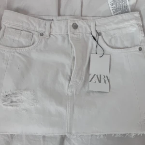 Vit jeanskjol låg midja från Zara med slitningar - Vit kort jeanskjol från Zara med coola slitningar och  kant nertill. knapp och dragkedja framtill. Storlek M men passar s prislappen är borta 