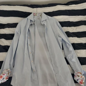 Ljusblå skjorta från Stenströms - Snygg ljusblå skjorta från Stenströms med fitted body-passform. Skjortan har blommigt tyg på insidan av kragen och manschetterna, samt klassisk krage och knappar framtill. Tillverkad i mjuk bomull som känns lyxig mot huden.