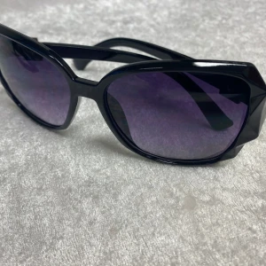 Snygg Dam  solglasögon  - Snygga solglasögon med svart och vinröd båge look i plast och coola geometriska former. Lila tonade glas och silverfärgad metall-detalj vid skalmarna. Perfekt accessoar för att lyfta din stil. Helt ny , 145kr/ st 